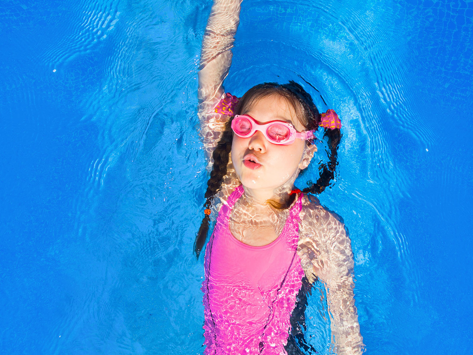 young girl swimming in a pink costume and goggles doing backstroke